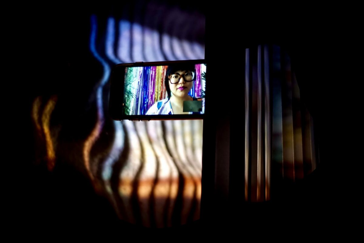 A woman looking at the viewer from a cellphone screen in a dark space
