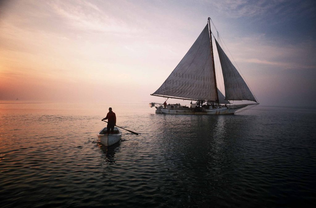 Man rowing dinghy away from sailboat