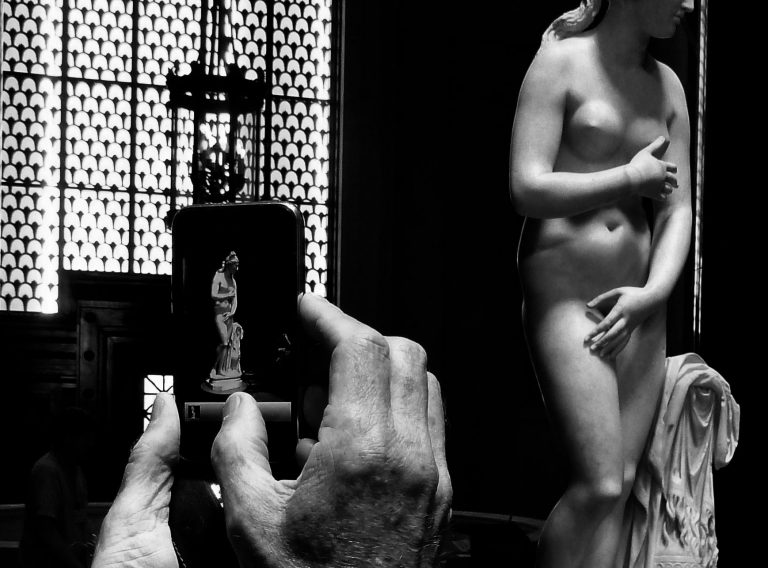 Black and white image of close up of hands holding an iPhone and making a picture of the Capitoline Venus