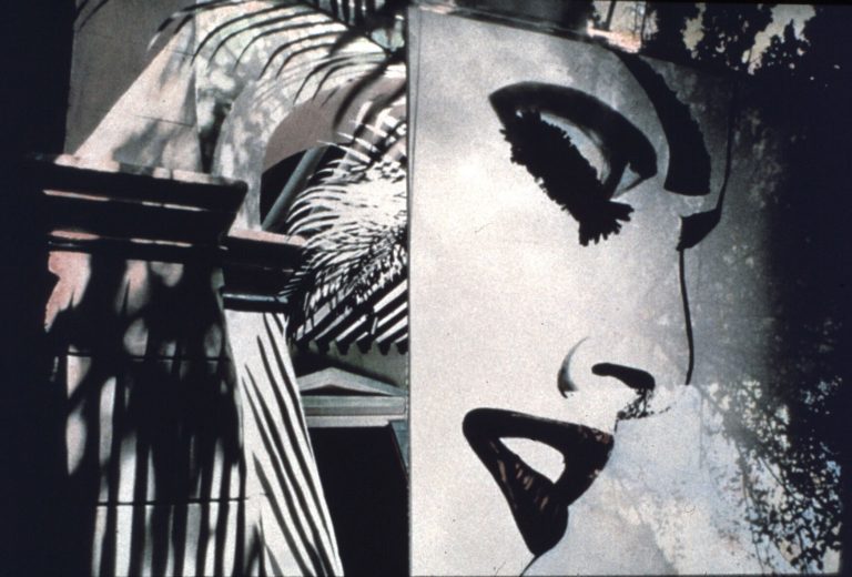 Black and white image of architectural detail, palm leaves, and woman's face on an advertisement
