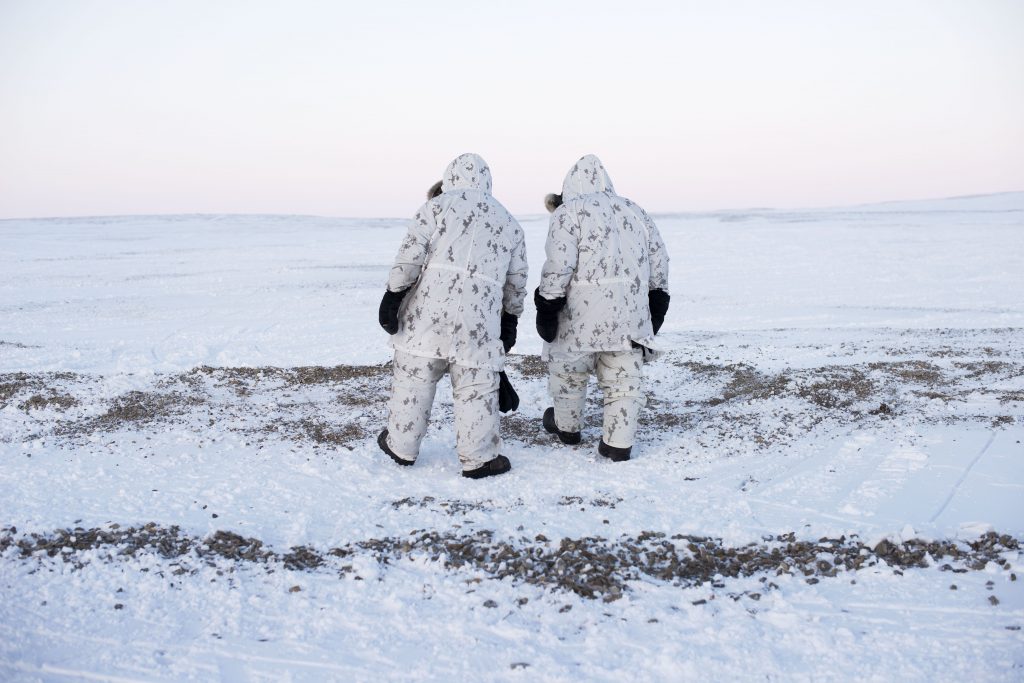 Two figures in winter camouflage walking across icy landscape
