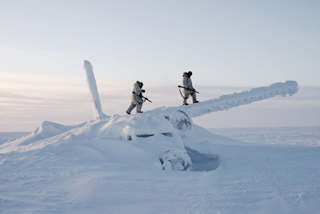 Two soldiers in winter gear walk on Ice covered plane wreckage