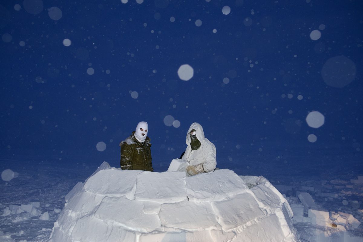 Two figures in balaclavas inside igloo at night