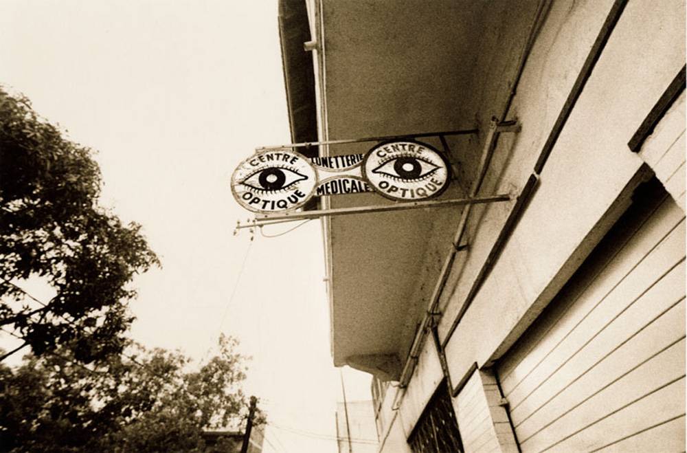 Sepia toned black and white photograph of a sign shaped like glasses