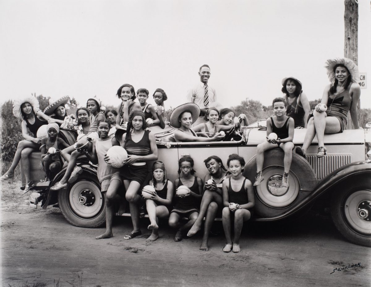 Black and white photograph of a group of children in bathing suits in and around a car