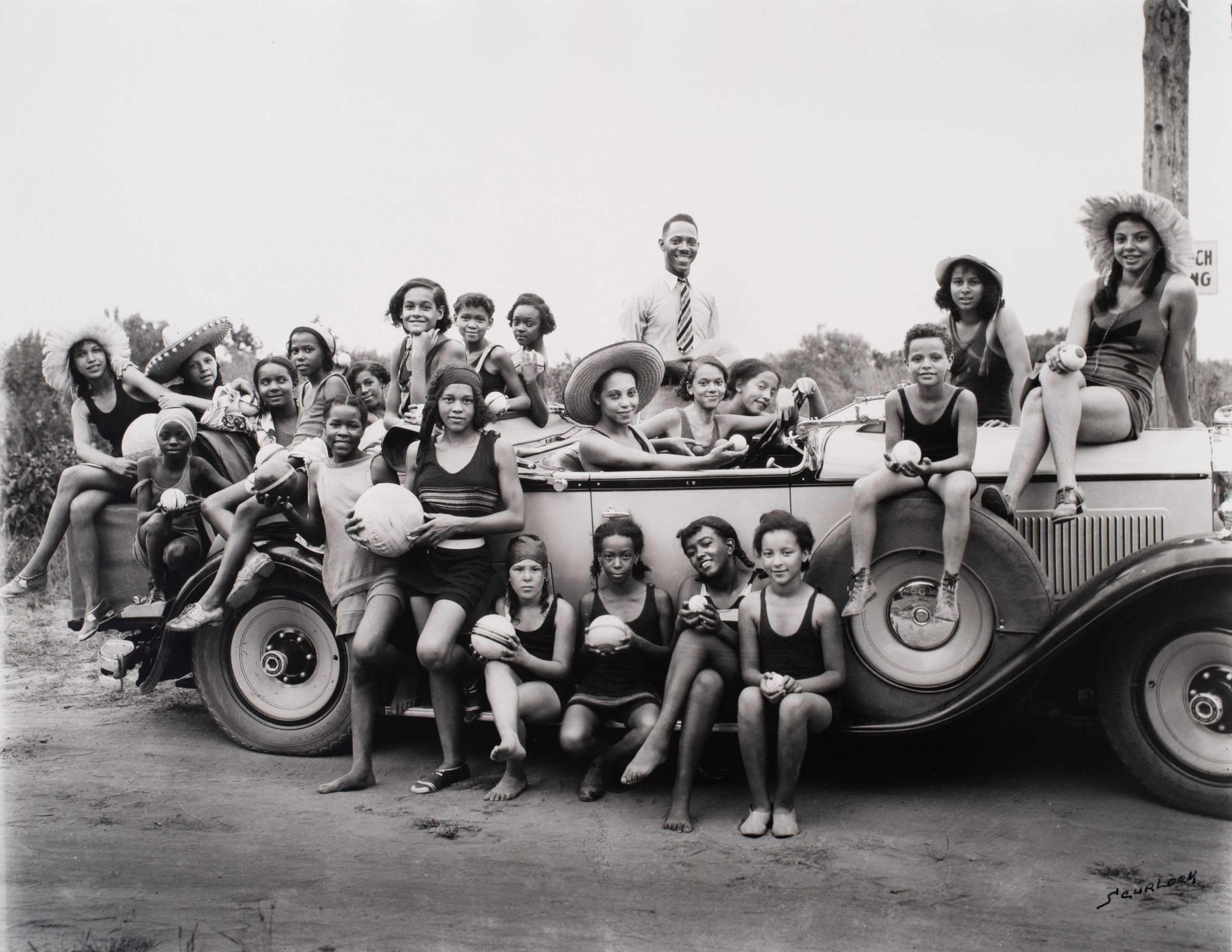 Black and white photograph of a group of children in bathing suits in and around a car
